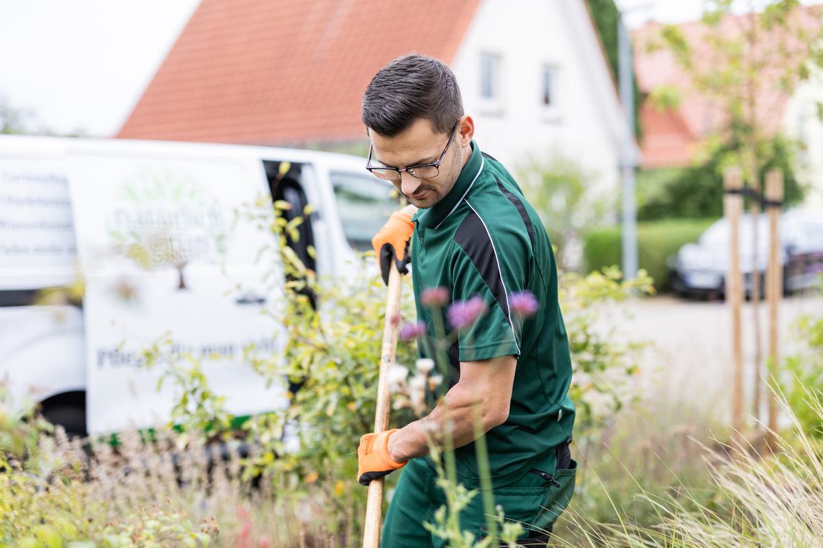 Benjamin Schink mit der Hacke im Beet, Transporter und Haus im Hintergrund